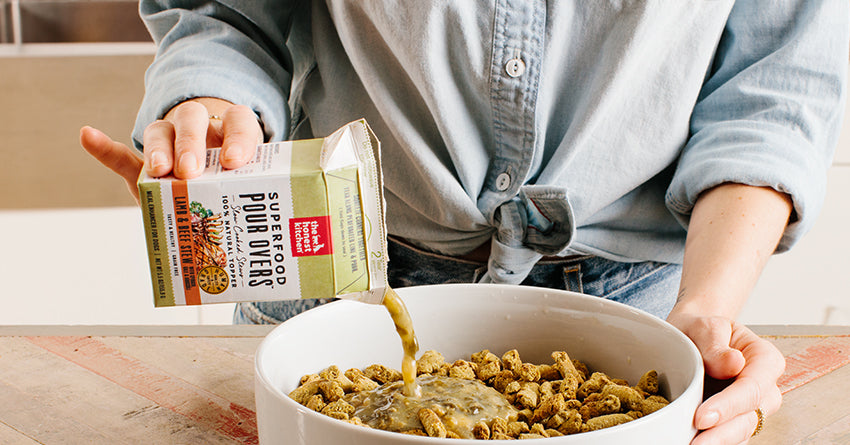 Woman pouring The Honest Kitchen's superfood pour overs over a bowl of dry food.