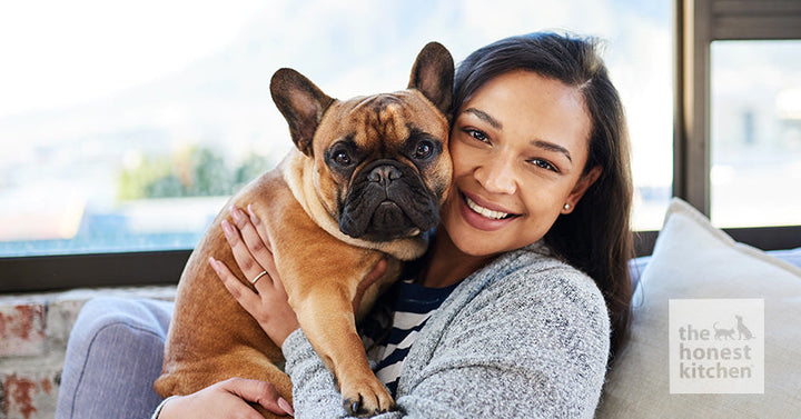 A woman holding her French Bulldog and smiling at the camera.