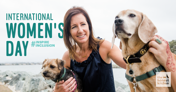 Lucy Postins on the beach with two dogs, one yorkie and one beagle, with International Women's Day Header