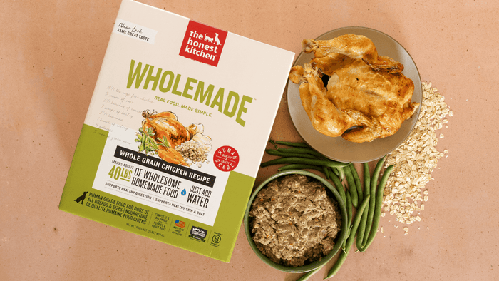 The Honest Kitchen Wholemade Whole Grain Chicken recipe pet food packaging with a bowl of food, green beans, and oats on a beige background. The Honest Kitchen's Healthy, High Quality, Human Grade Wholemade Dehydrated Dog Food. Helps Support Digestion.