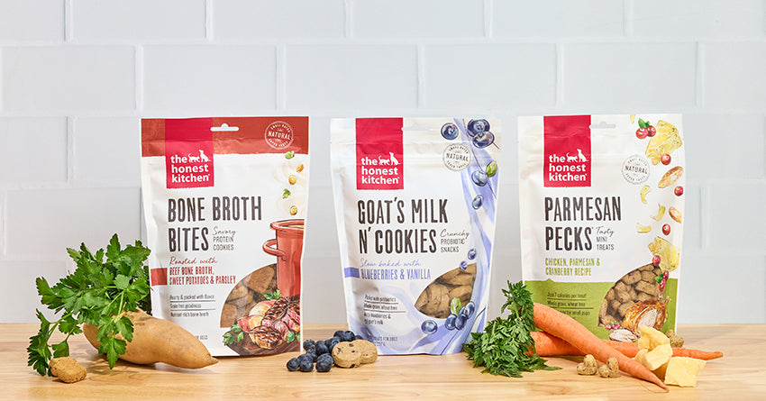 The Honest Kitchen's Cookie Treats for dogs on a butcher block counter with ingredients surrounding it. 