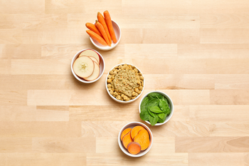 Ingredients on a kitchen table, such as apples, sweet potatoes, carrots, and spinach 