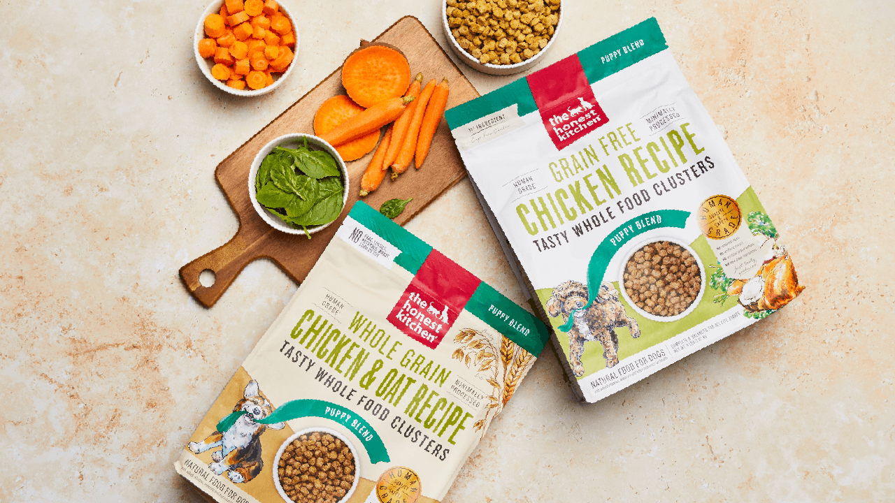 The Honest Kitchen's puppy clusters on a tan background surrounded by ingredients. Shop dry dog food clusters for puppies.