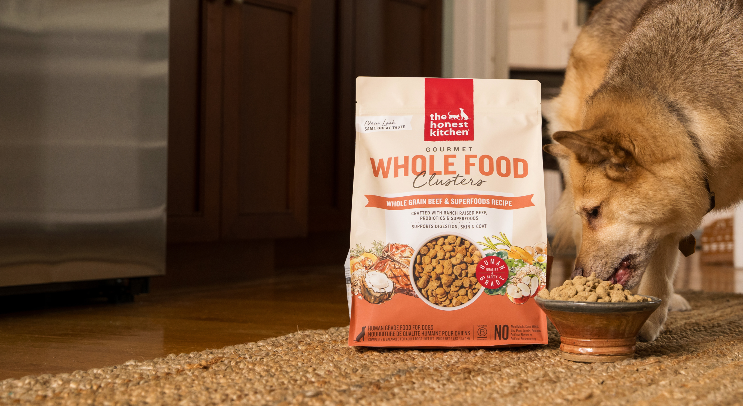 Dog eating from a bowl next to a bag of Whole Food Clusters pet food on a carpeted floor. Healthy, high quality, human grade dog and cat food from The Honest Kitchen.