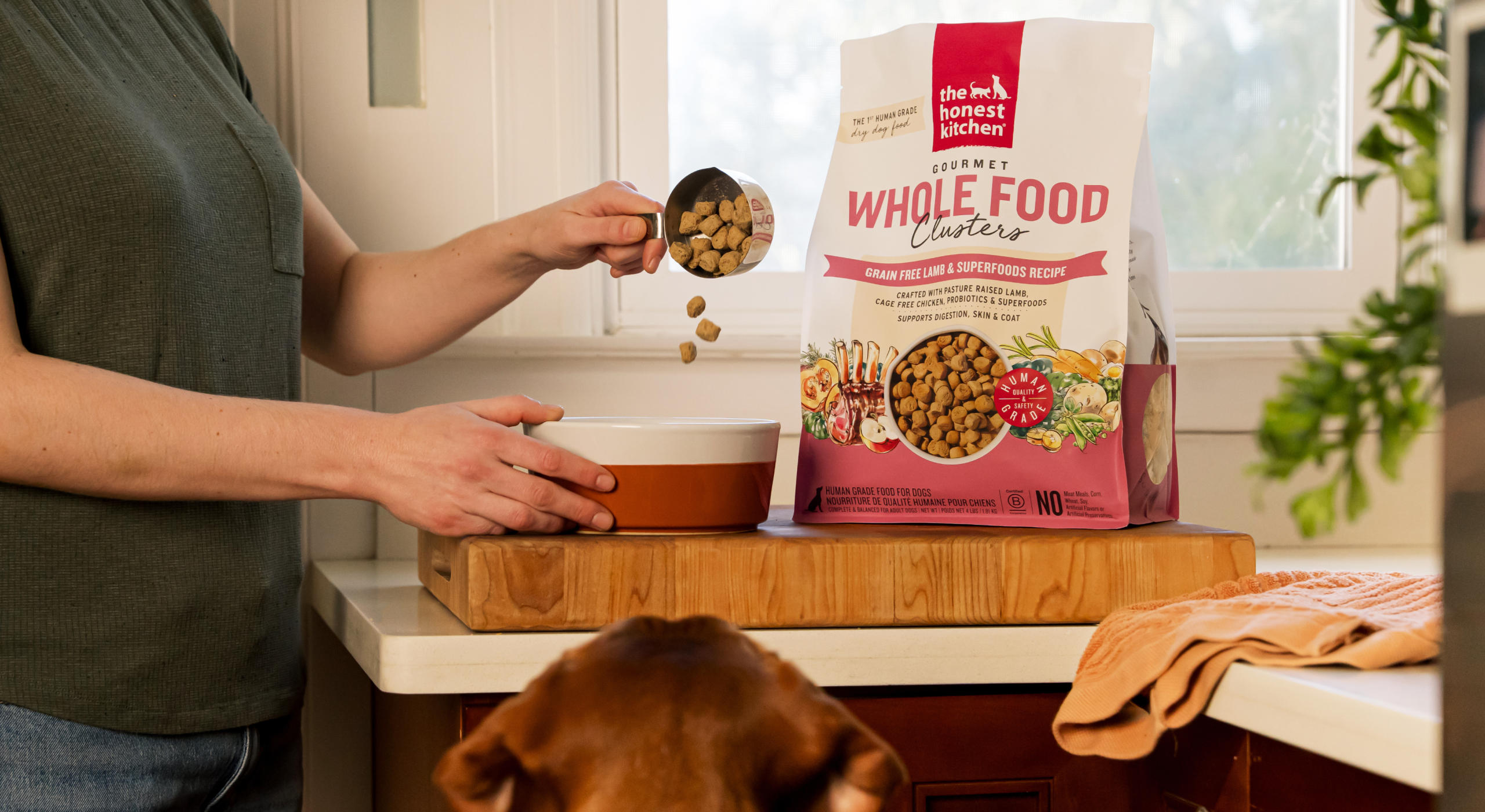 Woman pours a scoop of Lamb whole food clusters dry dog food. The Honest Kitchen healthy, high quality, human grade dry dog and cat food.