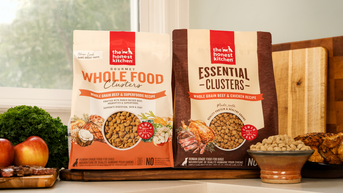 Two bags of The Honest Kitchen pet food on a table with ingredients in the background. About The Honest Kitchen.