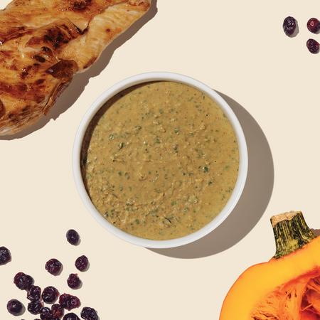 bowl of dehydrated cat food from the honest kitchen surrounded by ingredients like cage free chicken, cranberries and pumpkin to illustrate the ingredients included in the recipe.
