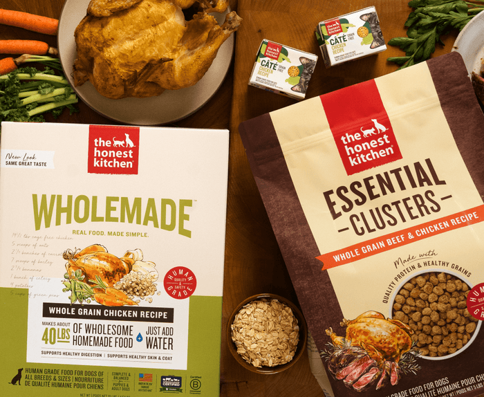 Two boxes of 'The Honest Kitchen' pet food on a wooden table with ingredients. Healthy, High Quality, Human Grade Food for Dogs and Cats from The Honest Kitchen.